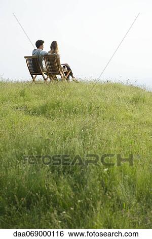 Stock Photograph - Couple sitting on chairs on top of hill looking at view. Fotosearch
