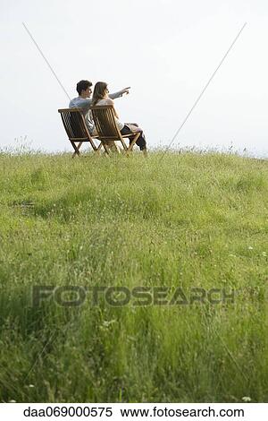 Couple sitting on chairs on top of hill looking at view, man pointing toward distance View Large Photo Image Stock Photography - Couple sitting on chairs on top of hill looking at view, man pointing toward distance. Fotosearch