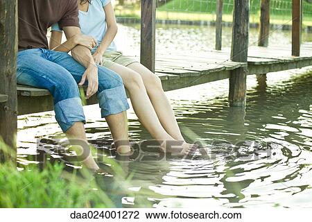 Couple sitting on dock, dangling legs in water, chest down View Large Photo Image Stock Image - Couple sitting on dock, dangling legs in water, chest down. Fotosearch