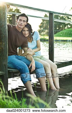 Couple sitting on dock, dangling legs in water, woman looking at camera, full length View Large Photo Image Stock Image - Couple sitting on dock, dangling legs in water, woman looking at camera, full length. Fotosearch