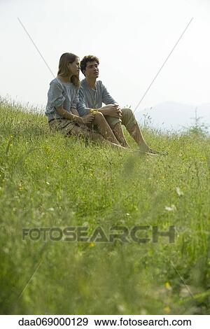 Stock Photo - Couple sitting on meadow looking at view. Fotosearch