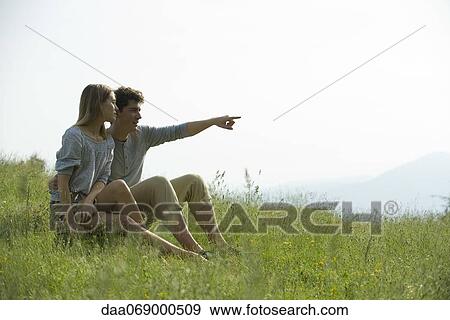 Couple sitting on meadow, man pointing toward distance View Large Photo Image Stock Photo - Couple sitting on meadow, man pointing toward distance. Fotosearch