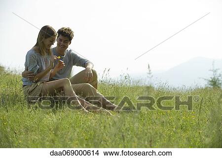 Couple sitting on meadow, woman picking flower petals View Large Photo Image Picture - Couple sitting on meadow, woman picking flower petals. Fotosearch