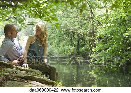Couple sitting on rock by river View Large Photo Image Stock Image - Couple sitting on rock by river. Fotosearch