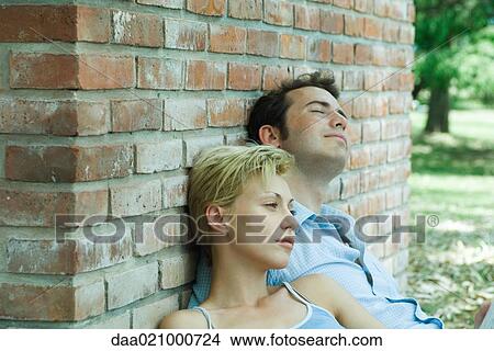 Couple sitting outdoors, leaning against brick wall View Large Photo Image Picture - Couple sitting outdoors, leaning against brick wall. Fotosearch