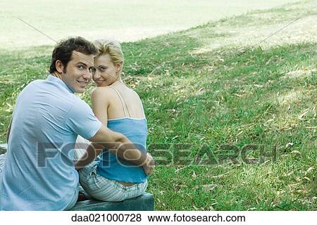 Couple sitting outdoors, looking over shoulders at camera View Large Photo Image Stock Photo - Couple sitting outdoors, looking over shoulders at camera. Fotosearch