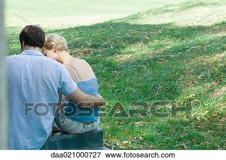 Stock Photo - Couple sitting outdoors, rear view. Fotosearch