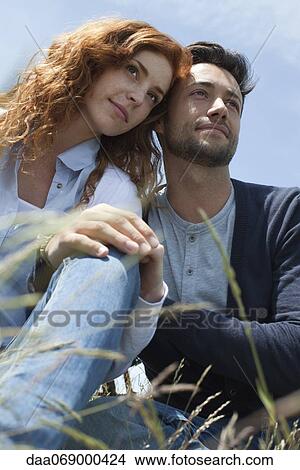 Picture - Couple sitting outdoors side by side with heads touching. Fotosearch
