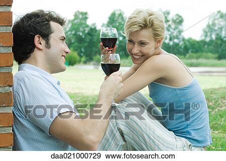 Couple sitting outdoors, toasting with glasses of red wine View Large Photo Image Stock Photo - Couple sitting outdoors, toasting with glasses of red wine. Fotosearch