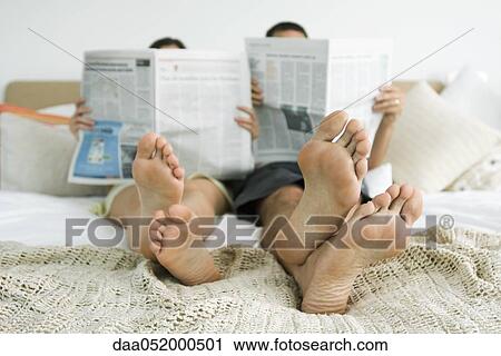 Stock Image - Couple sitting together on bed reading newspapers. Fotosearch