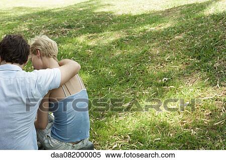 Stock Photography - Couple sitting together on grass, rear view. Fotosearch