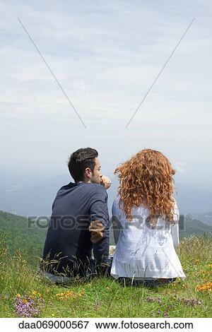 Couple sitting together on hilltop, looking at view View Large Photo Image Stock Photo - Couple sitting together on hilltop, looking at view. Fotosearch