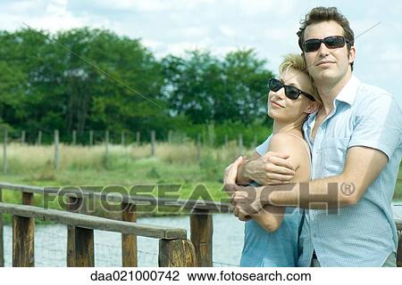 Couple standing by footbridge, man holding woman in his arms, both wearing sunglasses View Large Photo Image Stock Image - Couple standing by footbridge, man holding woman in his arms, both wearing sunglasses. Fotosearch