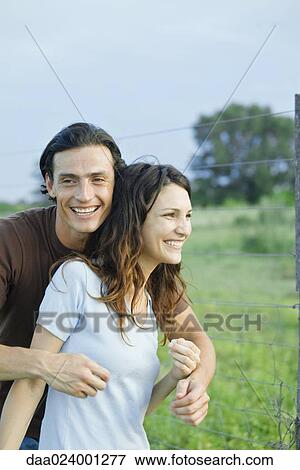 Stock Photo - Couple standing in rural setting, laughing, man standing behind woman. Fotosearch