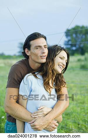 Couple standing in rural setting, laughing, man holding woman from behind View Large Photo Image Stock Photo - Couple standing in rural setting, laughing, man holding woman from behind. Fotosearch