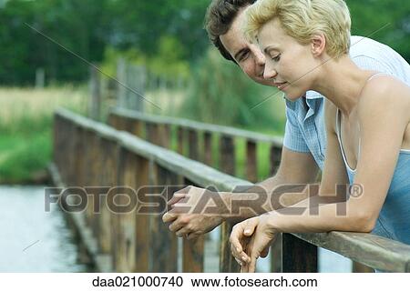 Couple standing on footbridge, leaning against rail, talking View Large Photo Image Stock Image - Couple standing on footbridge, leaning against rail, talking. Fotosearch