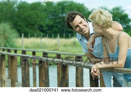 Couple standing on footbridge, leaning against rail, talking View Large Photo Image Stock Image - Couple standing on footbridge, leaning against rail, talking. Fotosearch