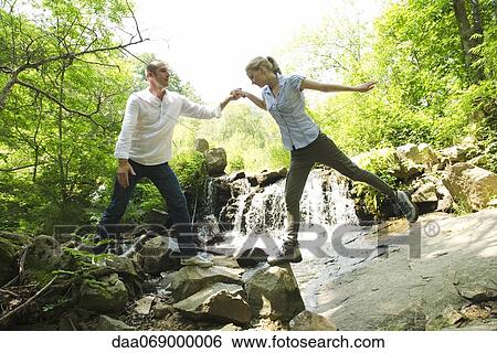 Stock Photograph - Couple standing on rocks by waterfall. Fotosearch