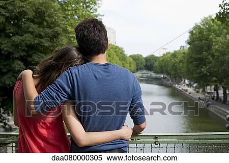 Stock Photography - Couple standing together on bridge, rear view. Fotosearch