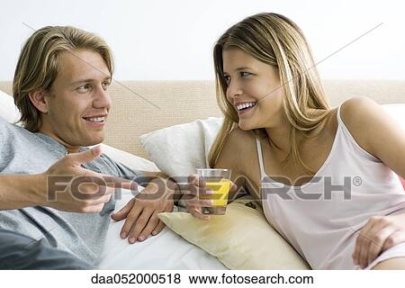 Stock Photo - Couple talking together in bed, woman holding glass of orange juice. Fotosearch