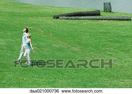 Couple walking across lawn, turning faces toward sun, full length, high angle view View Large Photo Image Stock Photograph - Couple walking across lawn, turning faces toward sun, full length, high angle view. Fotosearch