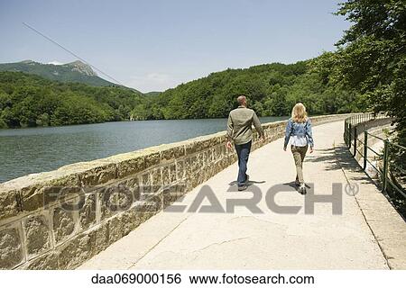 Stock Photograph - Couple walking by lake, rear view. Fotosearch