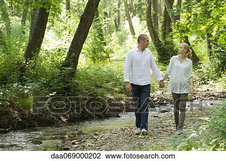 Stock Image - Couple walking by stream running through woods. Fotosearch