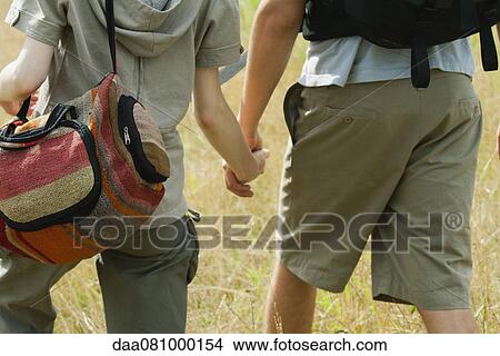 Couple walking in field holding hands, rear view View Large Photo Image Picture - Couple walking in field holding hands, rear view. Fotosearch