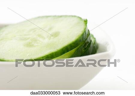 Stock Image - Cucumber slices piled in small dish, close-up. Fotosearch