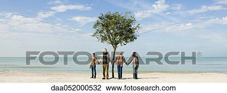 Stock Image - Ecology concept, group of people standing in front of tree, holding hands. Fotosearch