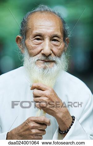 Picture - Elderly man holding long white beard in hands, portrait. Fotosearch