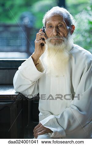 Stock Image - Elderly man wearing traditional Chinese clothing, using cell phone. Fotosearch