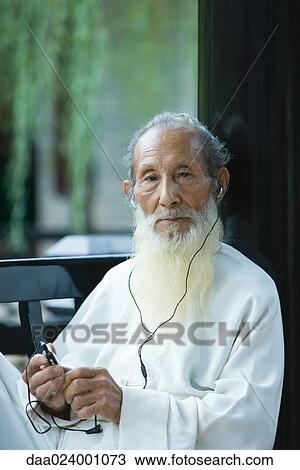Stock Image - Elderly man wearing traditional Chinese clothing, using MP3 player. Fotosearch