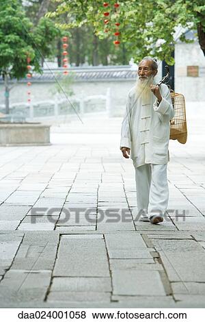 Stock Photo - Elderly man wearing traditional Chinese clothing carrying bird cage over shoulder. Fotosearch