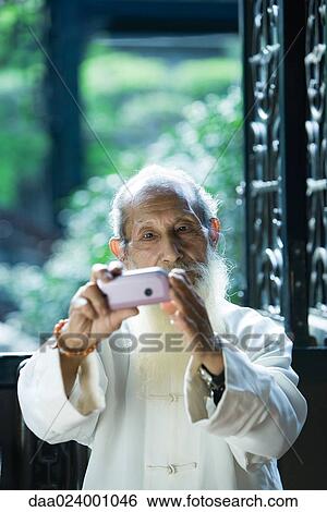 Stock Photograph - Elderly man wearing traditional Chinese clothing using camera phone. Fotosearch