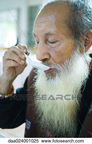 Stock Photography - Elderly man wearing traditional Chinese clothing, eating with soup spoon. Fotosearch