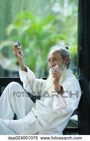 Stock Photography - Elderly man wearing traditional Chinese clothing, listening to MP3 player, moving arms and smiling. Fotosearch