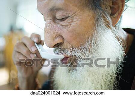 Elderly man with long beard eating with Chinese soup spoon View Large Photo Image Picture - Elderly man with long beard eating with Chinese soup spoon. Fotosearch