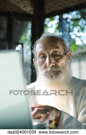 Stock Photo - Elderly man with long white beard using laptop. Fotosearch