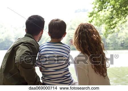 Family sitting together looking at lake, rear view View Large Photo Image Picture - Family sitting together looking at lake, rear view. Fotosearch