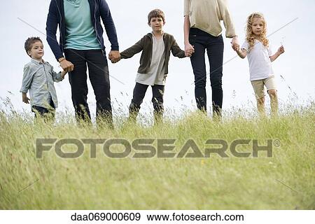 Stock Photo - Family walking hand-in-hand in field, cropped. Fotosearch