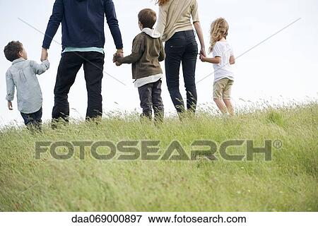 Stock Photo - Family walking together in field, rear view. Fotosearch