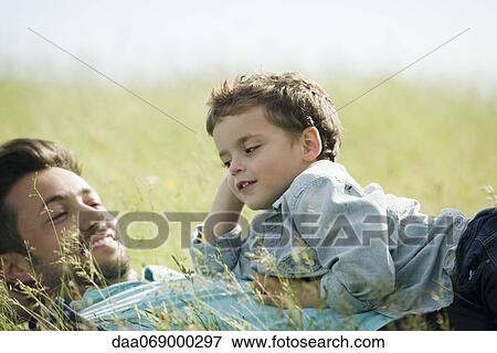 Father and young son lying down together in grass View Large Photo Image Stock Photo - Father and young son lying down together in grass. Fotosearch