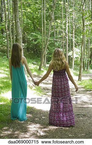 Stock Photography - Female friends walking hand in hand on path through woods. Fotosearch