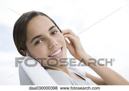 Female listening to earphones, smiling over shoulder at camera View Large Photo Image Stock Photo - Female listening to earphones, smiling over shoulder at camera. Fotosearch