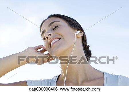 Stock Photograph - Female listening to earphones, smiling, eyes closed, low angle view. Fotosearch