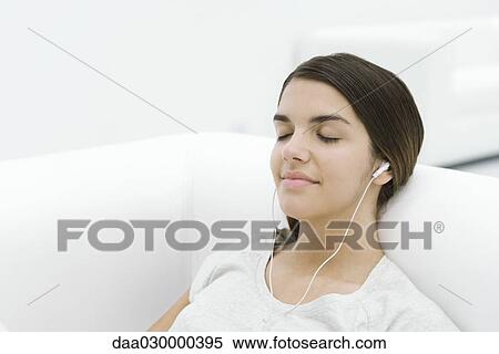 Female reclining on sofa, listening to earphones, eyes closed View Large Photo Image Stock Photography - Female reclining on sofa, listening to earphones, eyes closed. Fotosearch