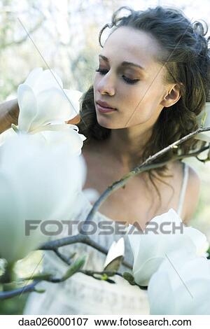 Stock Photo - Female smelling flowers, looking down, close-up. Fotosearch