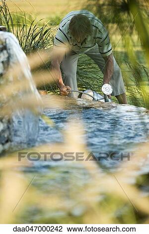 Filling watering can at stream View Large Photo Image Stock Image - Filling watering can at stream. Fotosearch