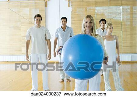 Stock Photo - Five adults standing in wellness center, woman in foreground holding fitness ball. Fotosearch